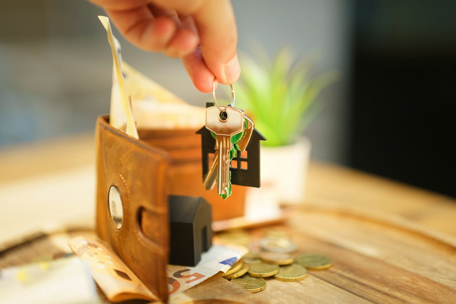 Main tenant un trousseau de clés à porte-clés maison au-dessus d'un portefeuille et de pièces de monnaie