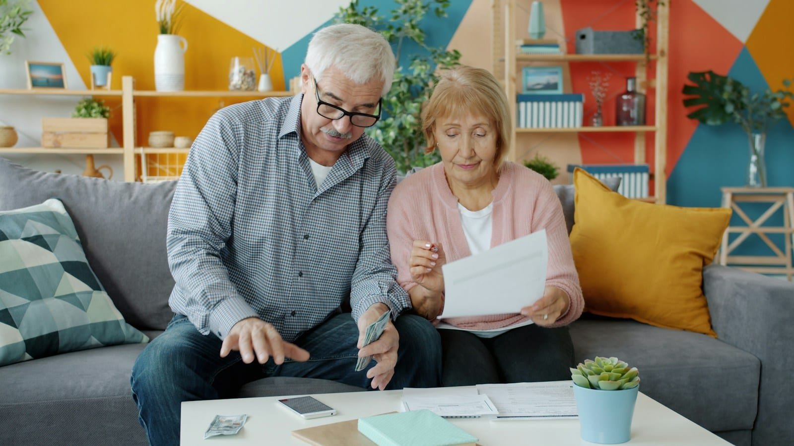 Couple de seniors relisant ensemble des documents sur la table de leur salon