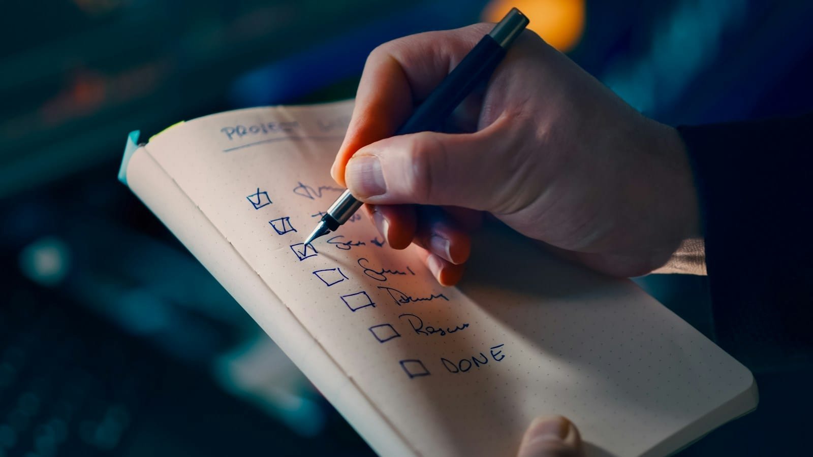 Main cochant les cases d'une liste de tâches manuscrite sur un carnet