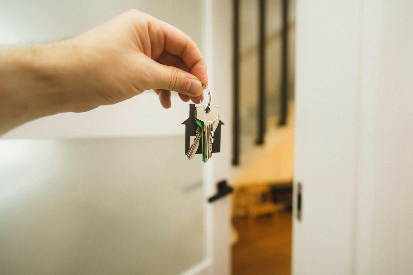 Main tenant une clé avec un porte-clés en forme de maison devant une porte entrouverte