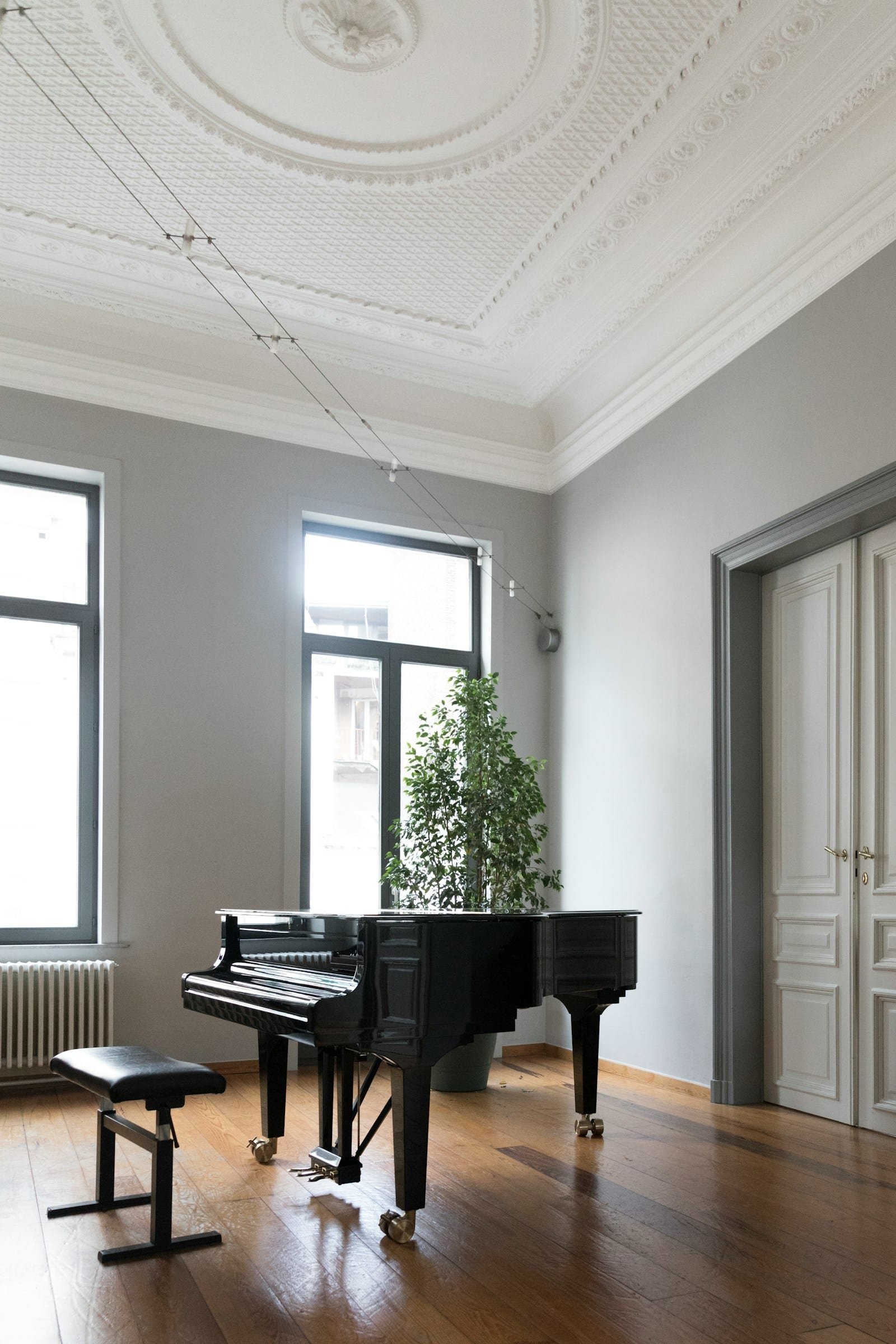 Piano à queue dans une pièce claire aux hautes fenêtres et moulures