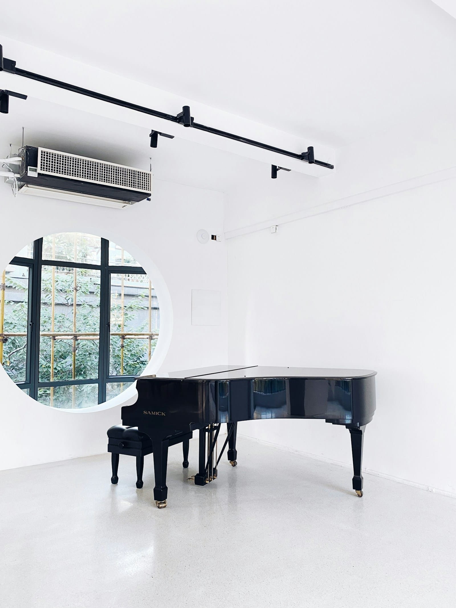 Piano à queue noir dans une pièce blanche éclairée par une fenêtre ronde