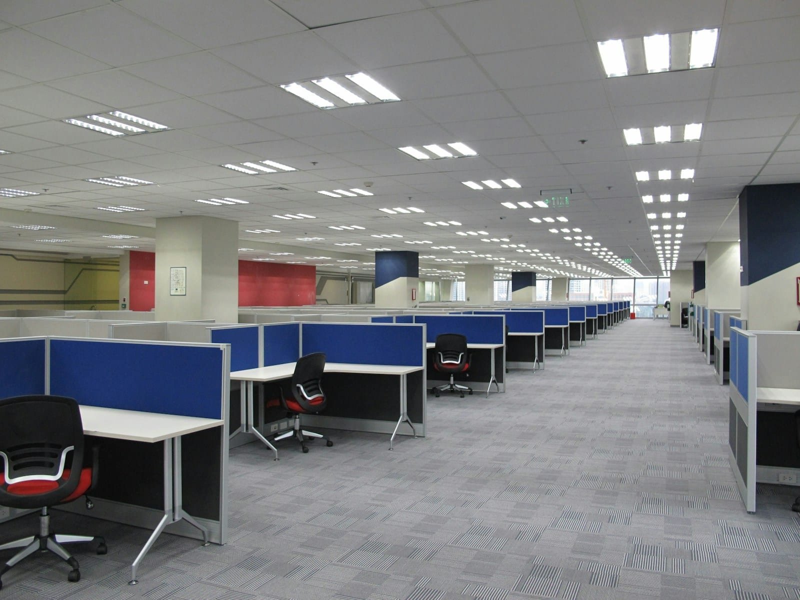 Transfert de bureaux : poste par poste, sans interruption d'activité Grand open space vide avec rangées de bureaux à cloisons bleues et fauteuils
